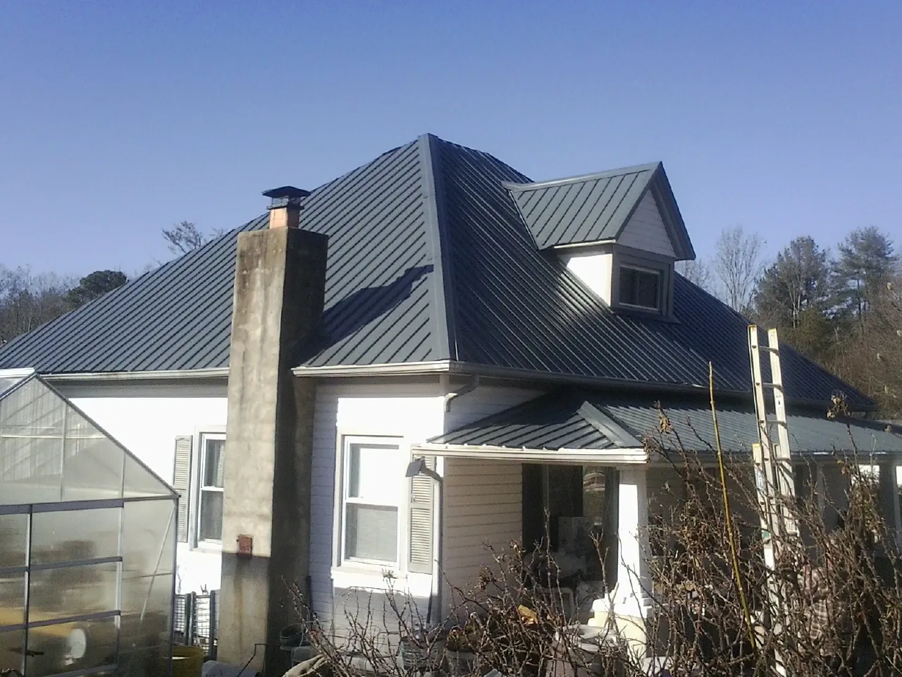 Dark blue standing seam metal roof on a white farmhouse with dormer — Slate & Tile Roof Repair by Roofing Brothers in Rising City