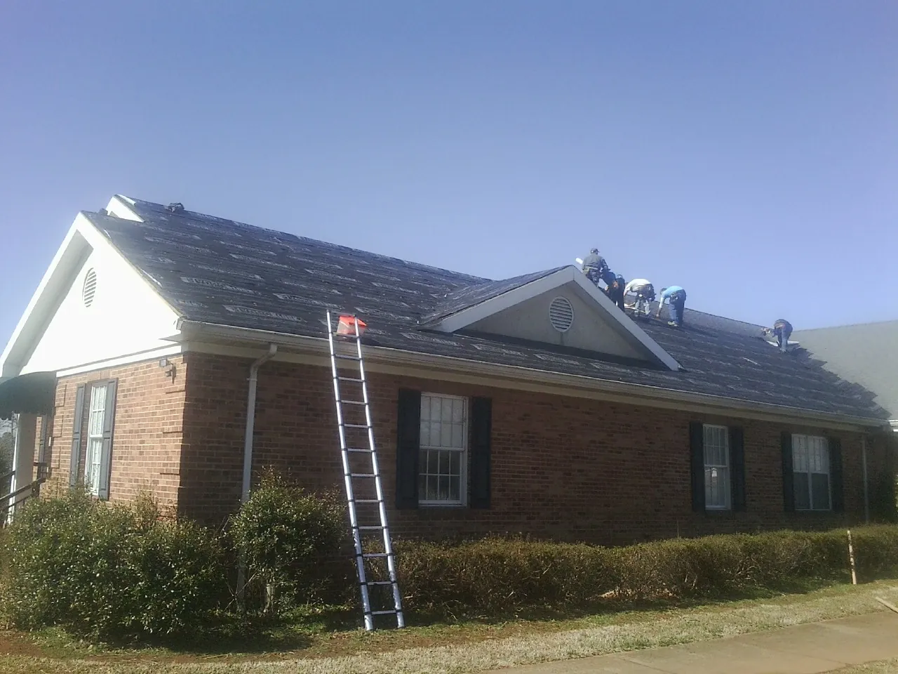 Crew tearing shingles off a brick ranch roof with a ladder set — Emergency Roof Repair work by our crew in Rising City