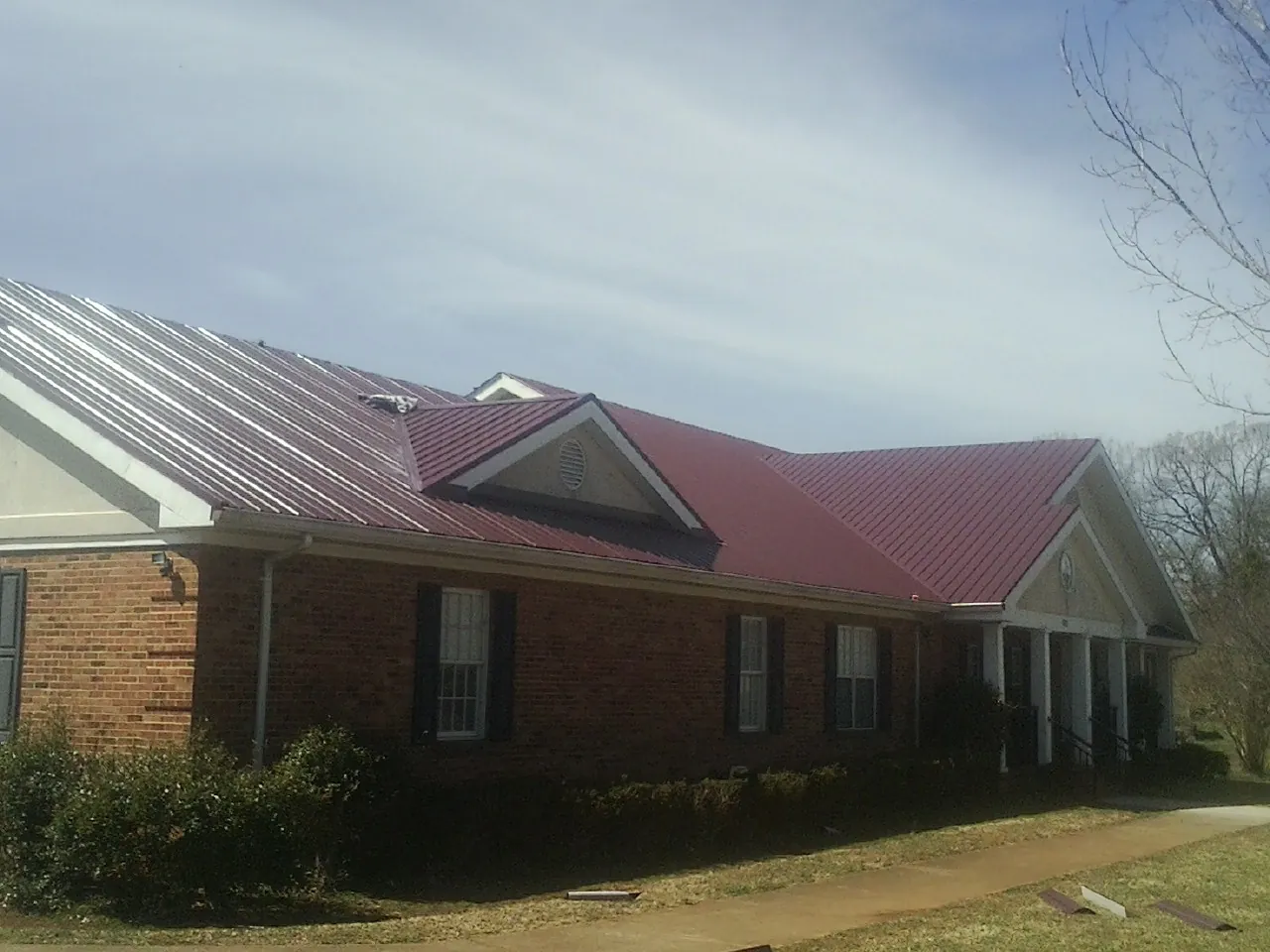 Red metal roof with gabled entries on a long brick building, from a Hail Damage Roof Repair job in Rising City