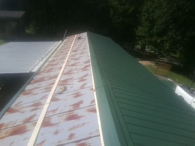 Old rusted panels beside newly installed green metal roofing — Wind Damage Roof Repair by Roofing Brothers in Rising City