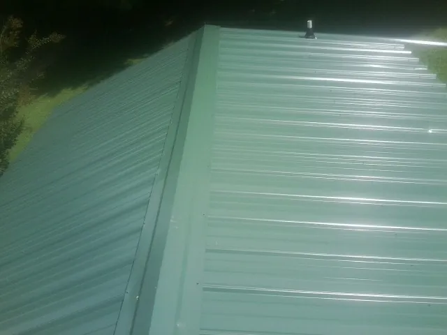 New green metal panels meeting at the ridge of a roof — Flat Roof Repair work by our crew in Rising City