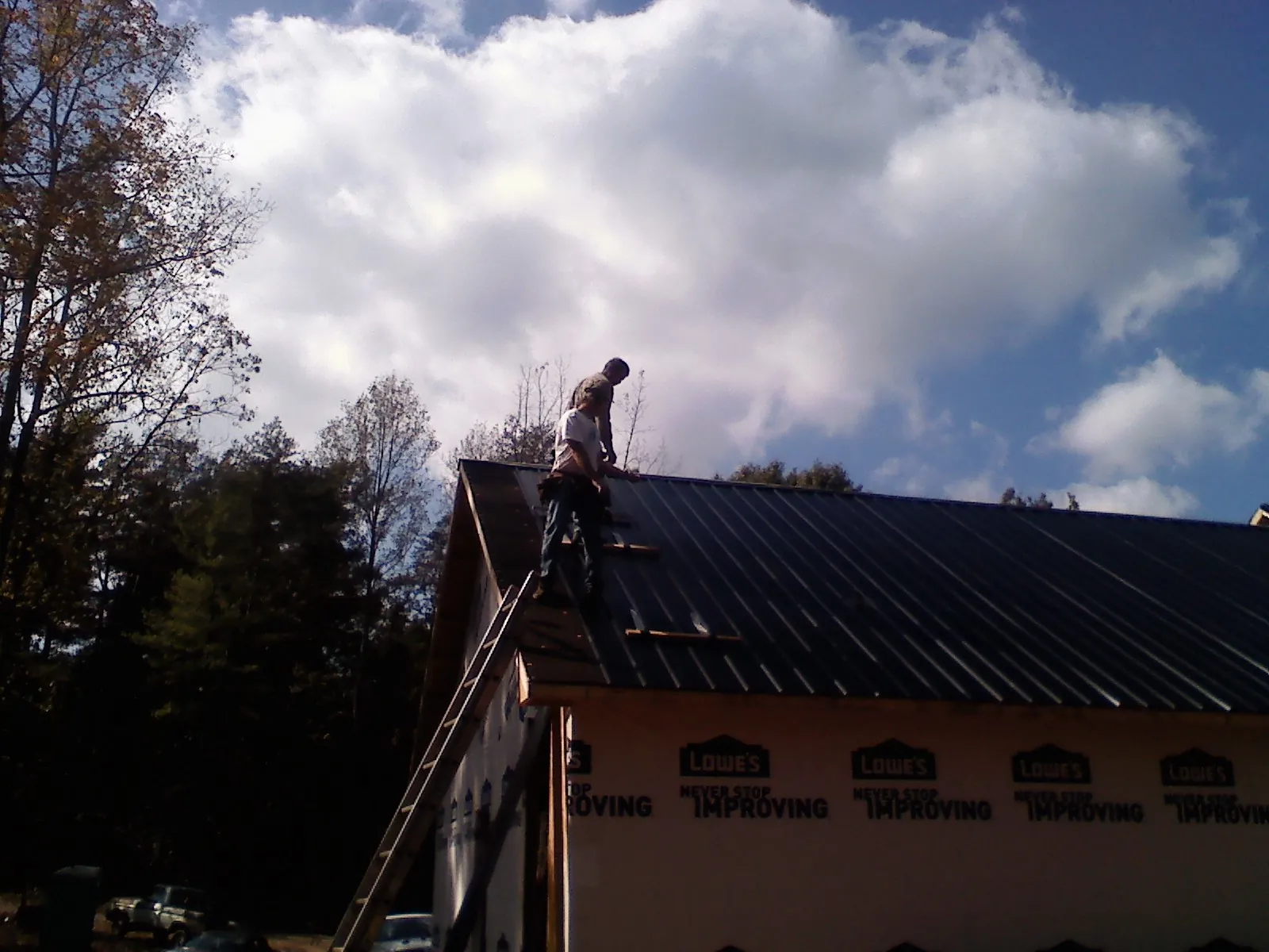 Roofer fastening dark metal panels high against a cloudy sky, from a Roof Inspection job in Rising City