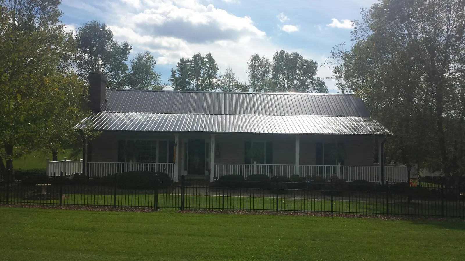 Gray metal roof on a brick ranch with a full width front porch — Gutter Guard Installation work by our crew in Rising City