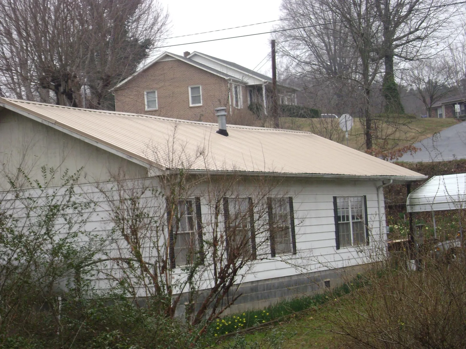 Tan metal roof on a white sided house set into a hillside — Commercial Roofing by Roofing Brothers in Rising City