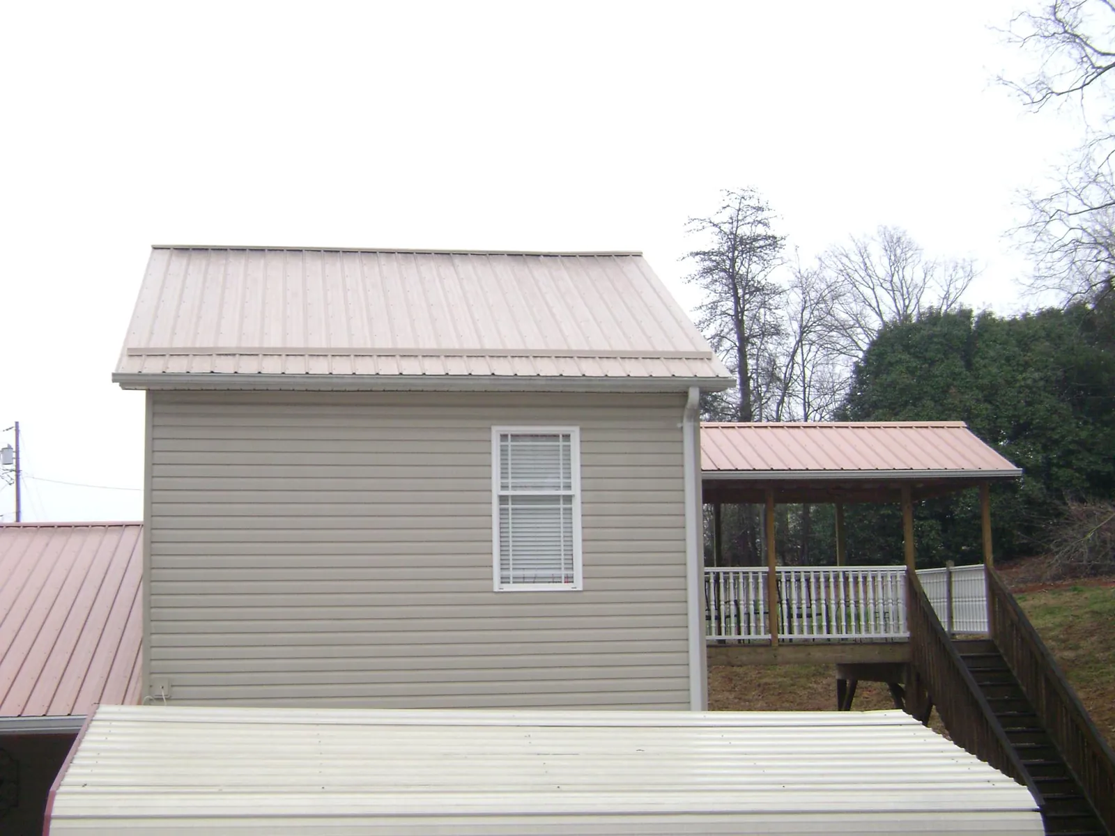 Tan metal roofs on a two story addition and attached porch, from a Roof Replacement job in Rising City