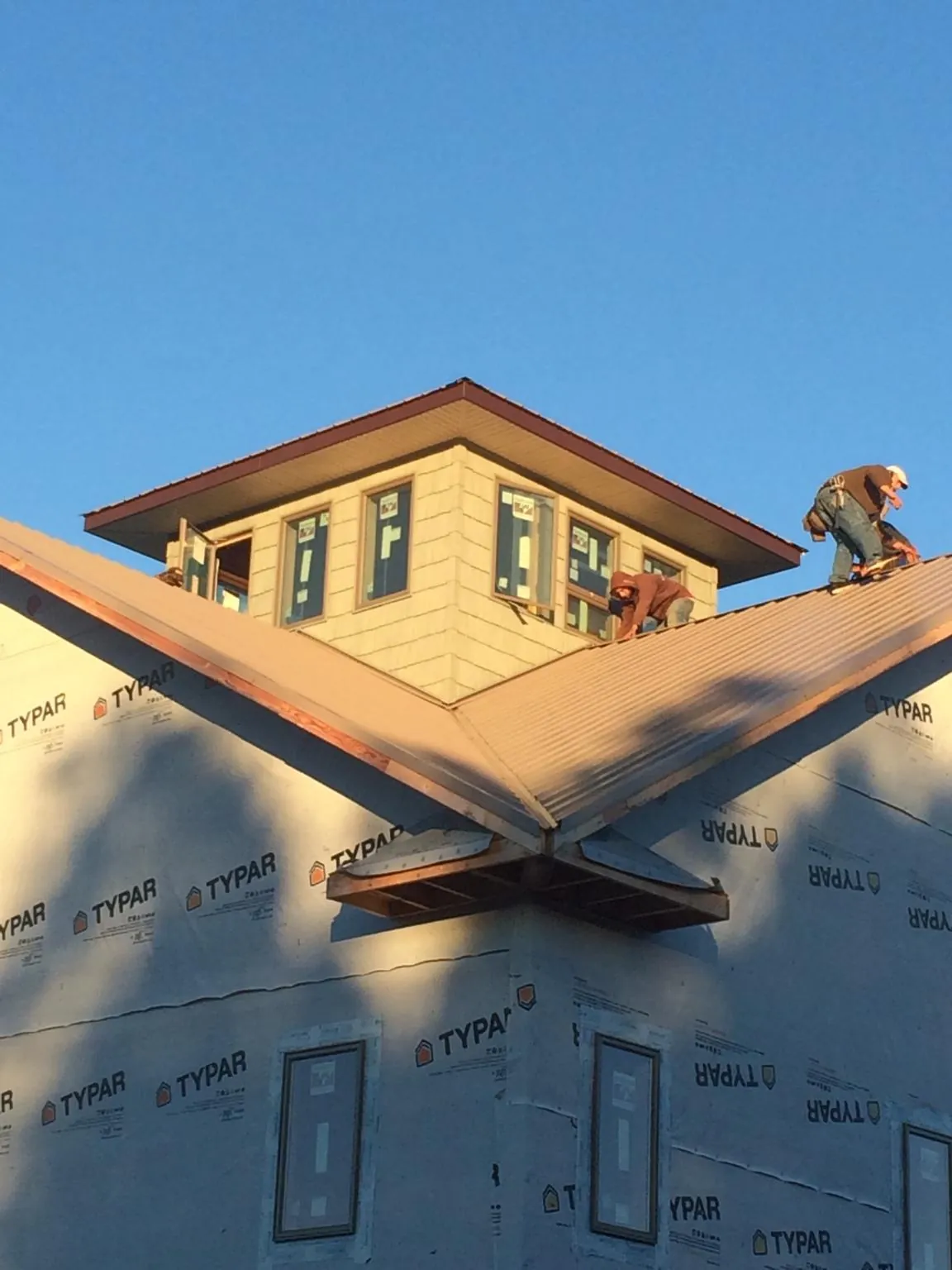 Roofers working around a rooftop cupola on a new metal roof at sunset — Roof Waterproofing in Rising City by Roofing Brothers